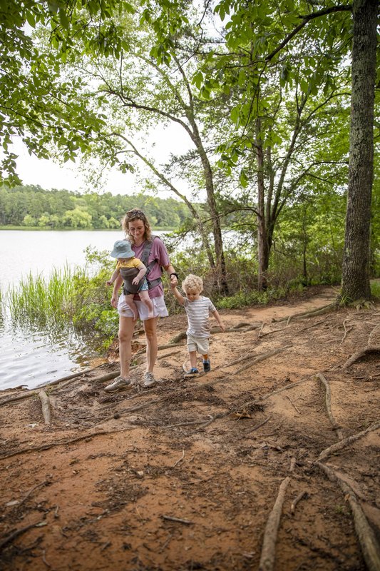 Mother and two kids hiking on dirt trail with tall trees next to lake in Tyler State Park