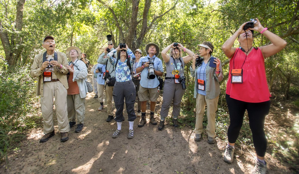 Group of people with binoculars and cameras on dirt trail