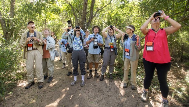 Group of people with binoculars and cameras on dirt trail