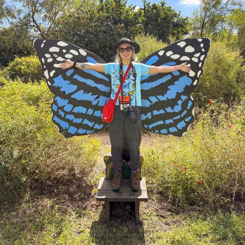 Woman standing with arms wide in front of blue and white butterfly wings at a photo stop.