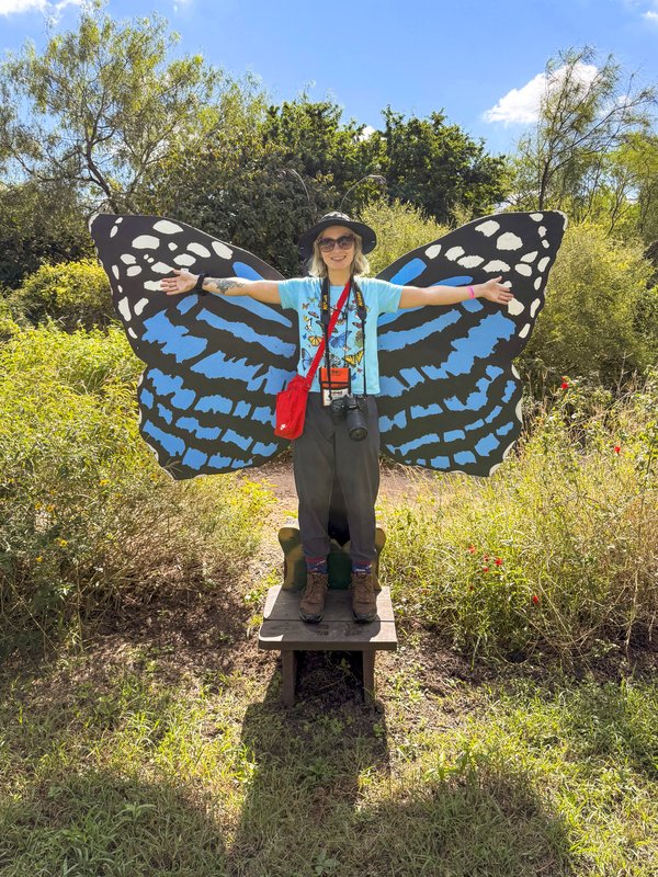 Woman standing with arms wide in front of blue and white butterfly wings at a photo stop.
