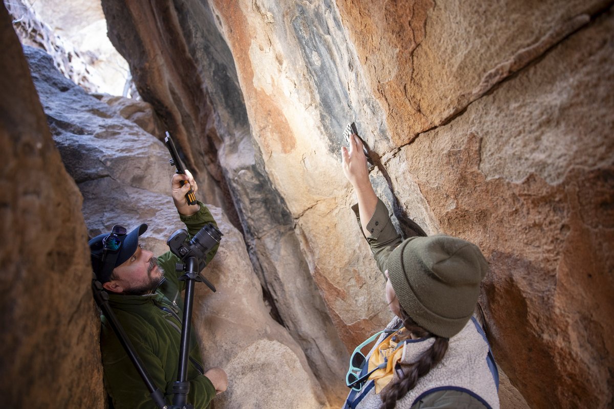 Two archeologists in-between boulders photographing pictographs on rock