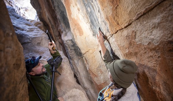 Two archeologists in-between boulders photographing pictographs on rock
