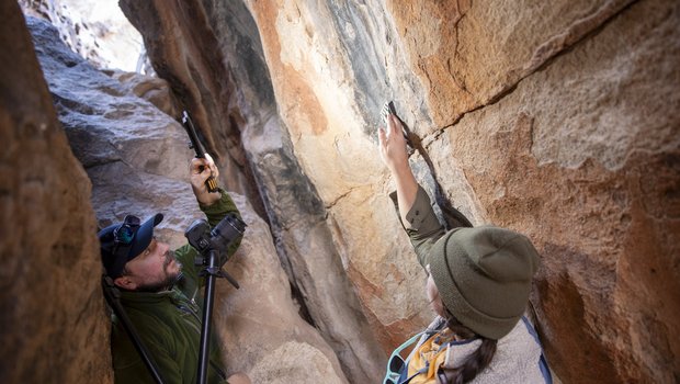 Two archeologists in-between boulders photographing pictographs on rock