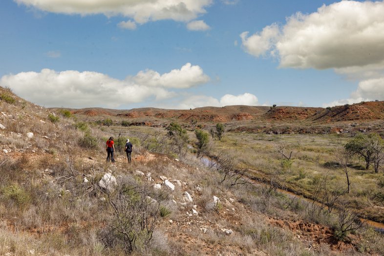 Two hikers on red dirt trail next to creek
