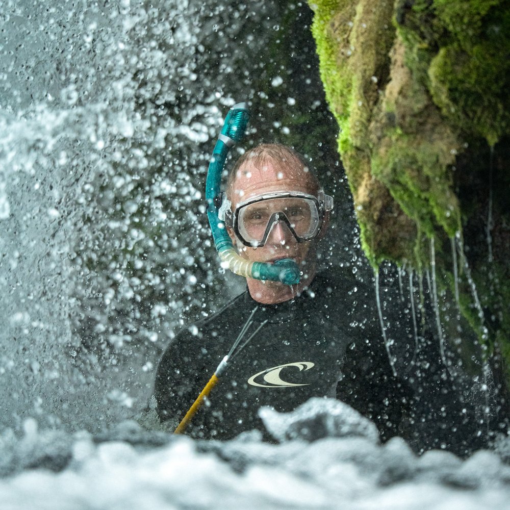 A person under a waterfall on the San Marcos River.