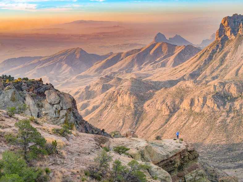 A hiker at the edge of a cliff on the Lost Mine Trail viewing mountains at Big Bend.