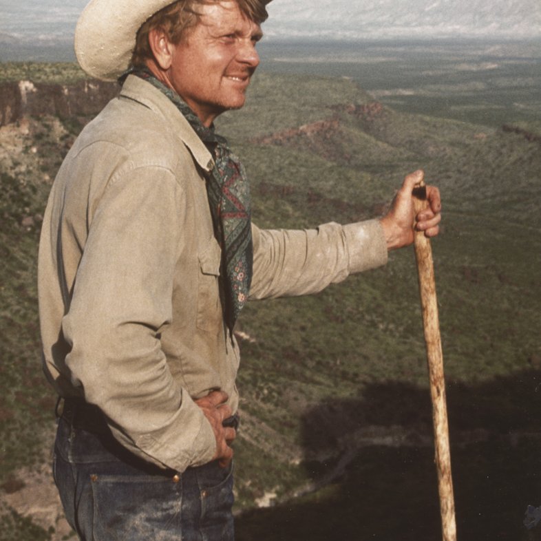 Scooter Cheatham, in a cowboy hat and jeans, stands and looks to the left from Chambers Trek