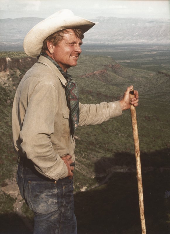 Scooter Cheatham, in a cowboy hat and jeans, stands and looks to the left from Chambers Trek