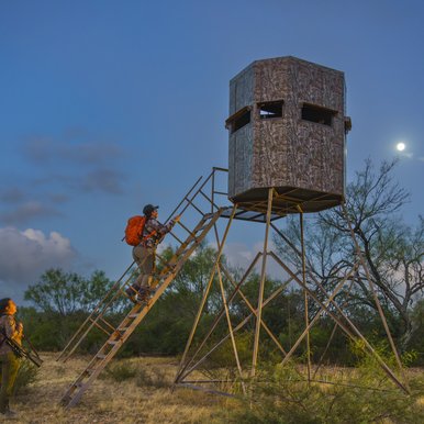 As dawn rises, two hunters climb the steps up into their deer blind