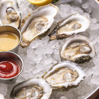 Oysters served on the half shell, resting on ice next to cocktail sauce and melted butter