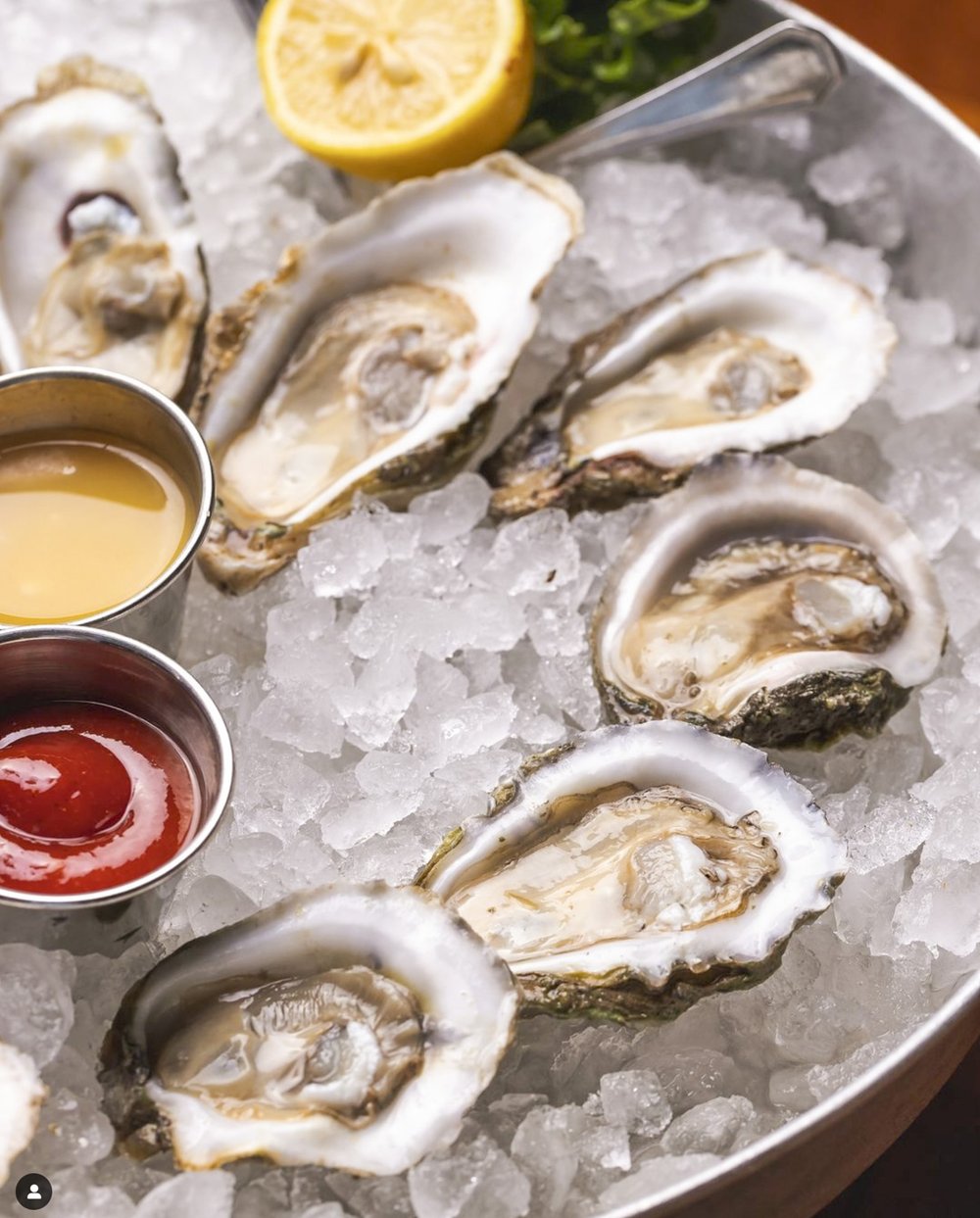 Oysters served on the half shell, resting on ice next to cocktail sauce and melted butter