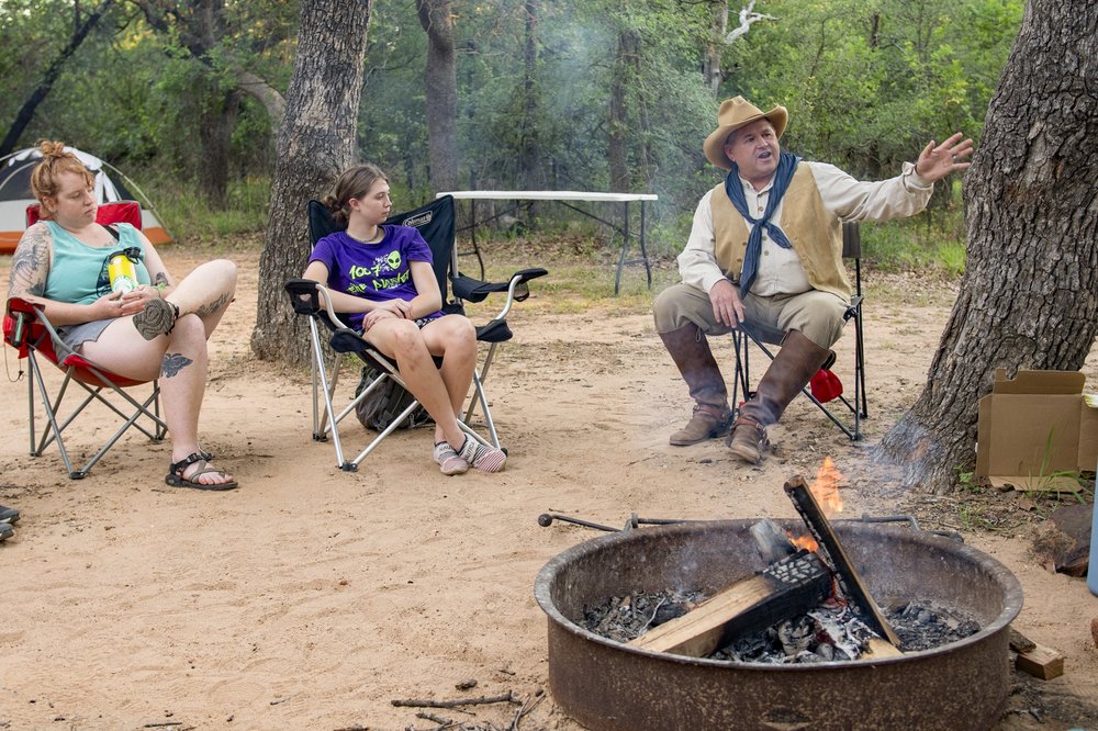 A cowboy poet entertains his listeners as they sit in camp chairs