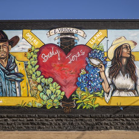 a colorful mural depicts a cowboy and cowgirl standing on either side of a large red heart on a wall in Brady Texas