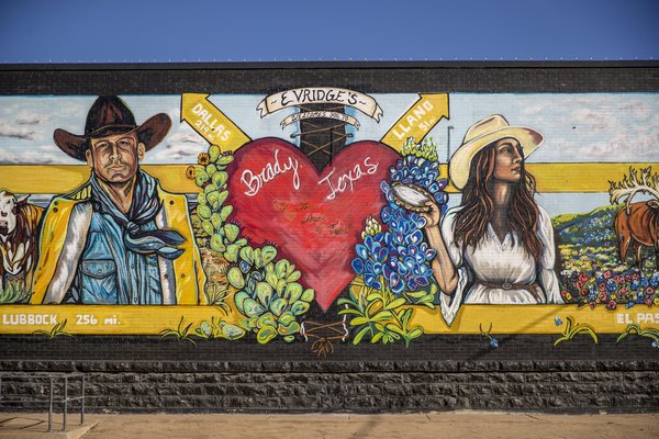 a colorful mural depicts a cowboy and cowgirl standing on either side of a large red heart on a wall in Brady Texas