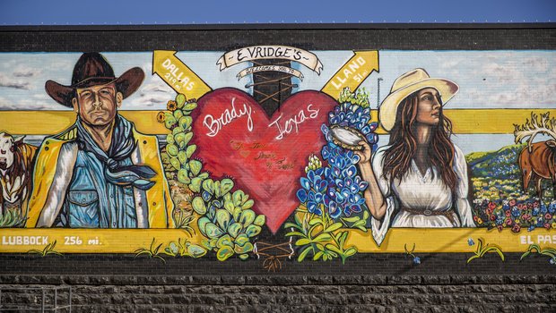 a colorful mural depicts a cowboy and cowgirl standing on either side of a large red heart on a wall in Brady Texas
