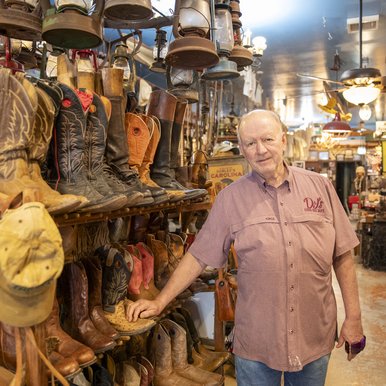 An older gentleman in a red shirt poses in front of rows of cowboy boots on display