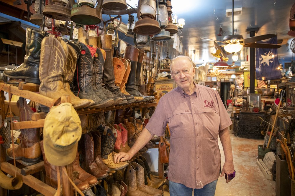 An older gentleman in a red shirt poses in front of rows of cowboy boots on display