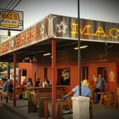 A crowd sits at picnic-style tables outside Macs BBQ in Brady