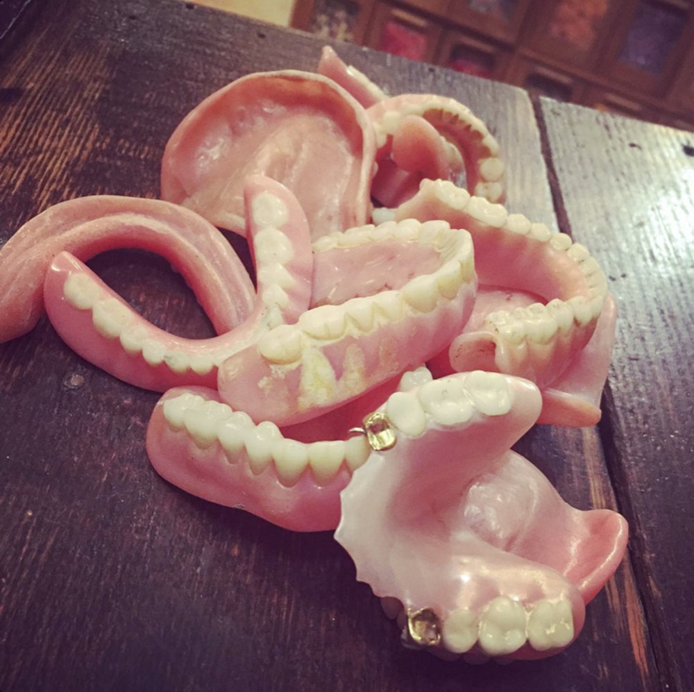 Several pair of old dentures and false teeth are displayed in random order on a table