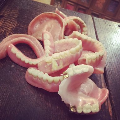 Several pair of old dentures and false teeth are displayed in random order on a table