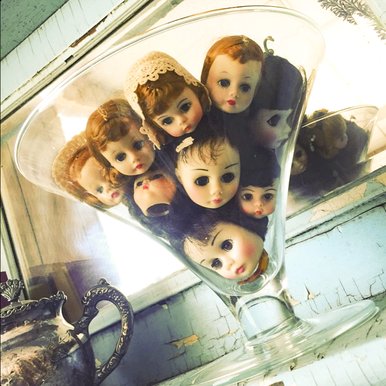 a collection of tiny doll heads stacked together inside a martini glass
