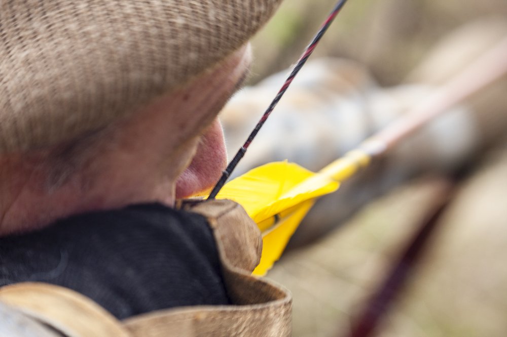 A person pulling back a yellow arrow in a traditional bow for hunting.