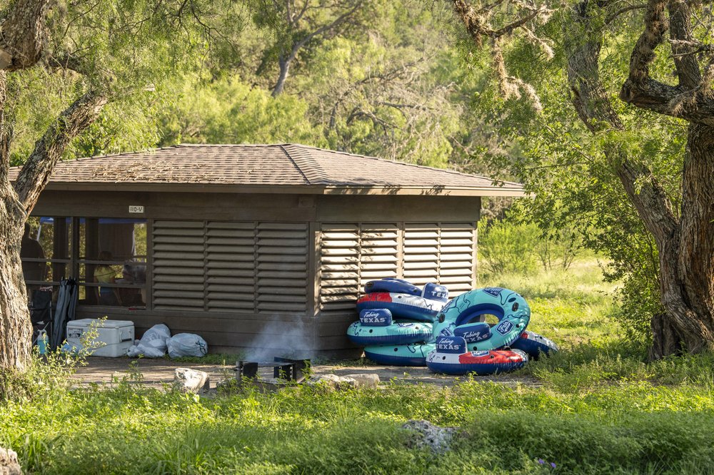 A screened shelter a Garner State Park with cooler and inner tubes outside.