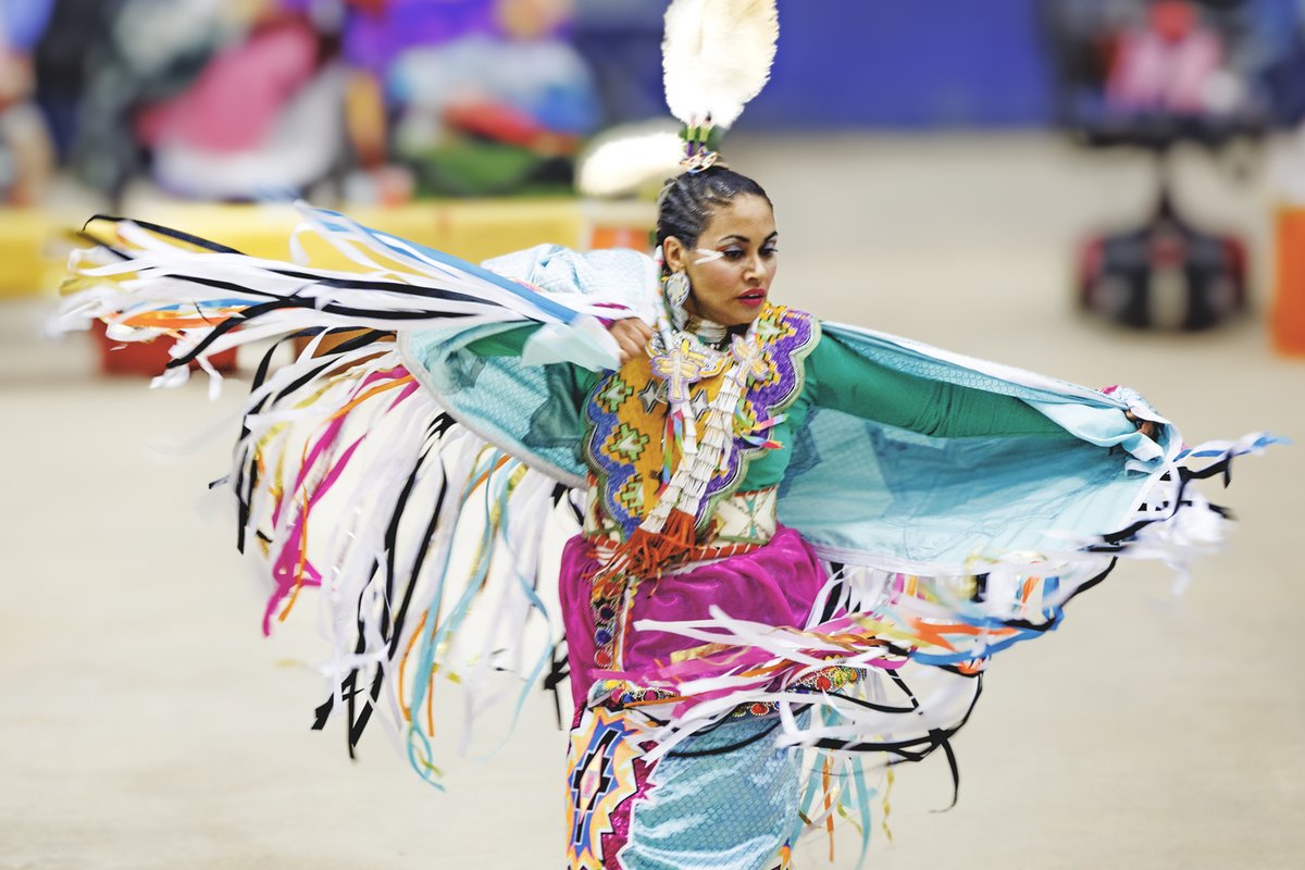 Native American woman dressed in colorful cultural attire dancing at the annual Powwow.