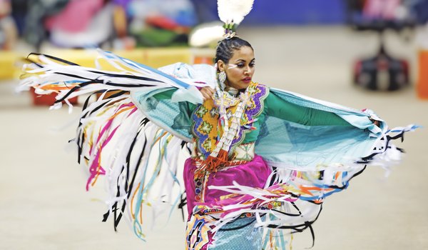Native American woman dressed in colorful cultural attire dancing at the annual Powwow.