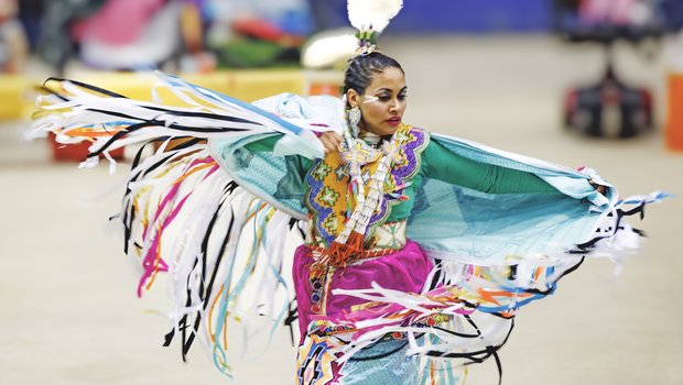 Native American woman dressed in colorful cultural attire dancing at the annual Powwow.