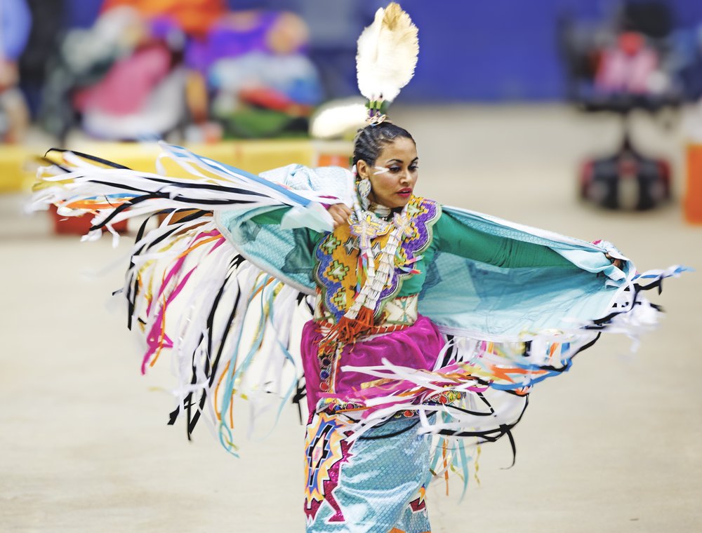 Native American woman dressed in colorful cultural attire dancing at the annual Powwow.