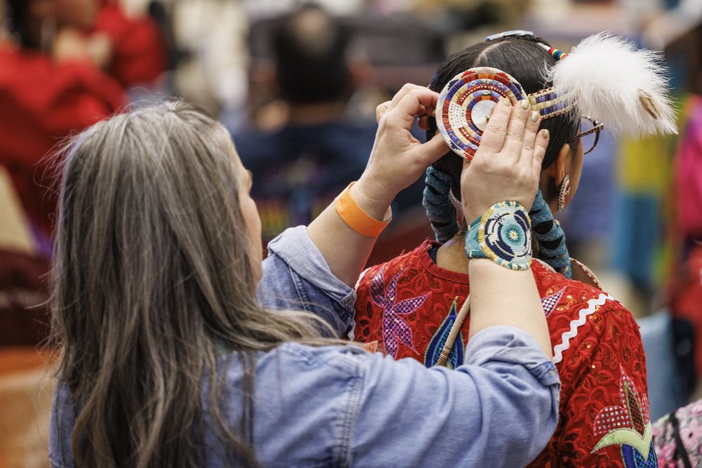 A person helping a dancer attach their headwear.