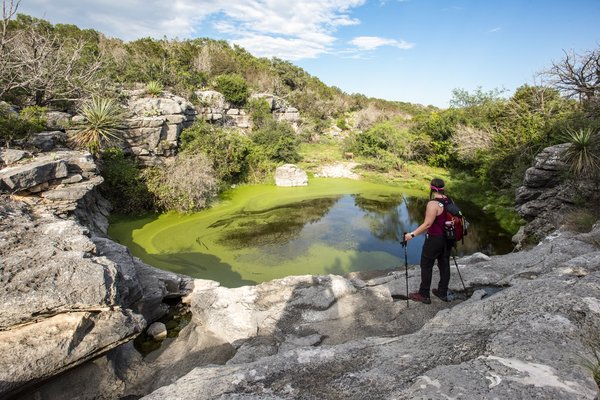 A woman takes a break from hiking to admire a waterhole at Colorado Bend State Park