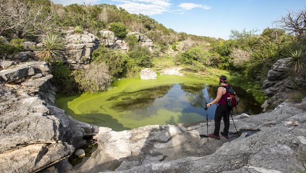 A woman takes a break from hiking to admire a waterhole at Colorado Bend State Park