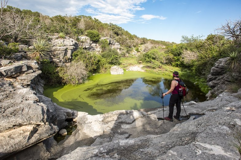 A woman takes a break from hiking to admire a waterhole at Colorado Bend State Park