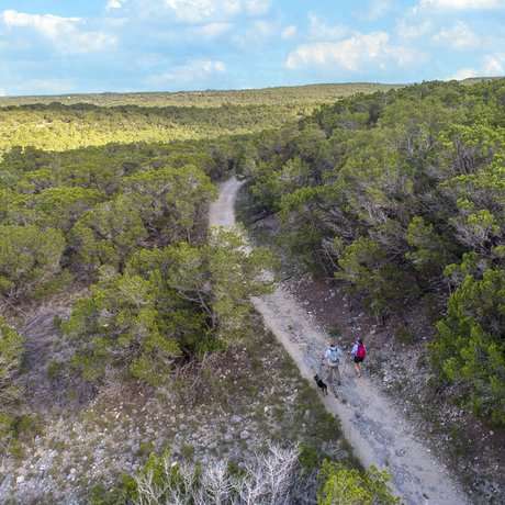 A man and woman hike along a trail with their dog at Pedernales Falls State Park.
