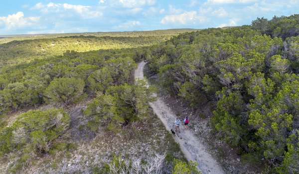 A man and woman hike along a trail with their dog at Pedernales Falls State Park.