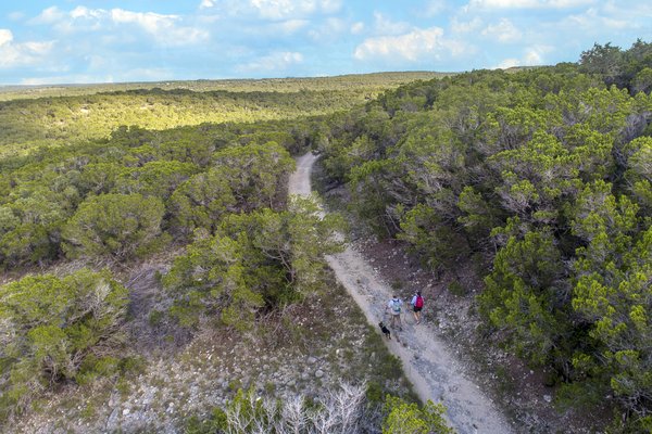 A man and woman hike along a trail with their dog at Pedernales Falls State Park.