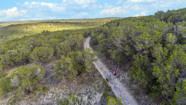 A man and woman hike along a trail with their dog at Pedernales Falls State Park.