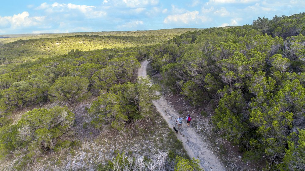 A man and woman hike along a trail with their dog at Pedernales Falls State Park.