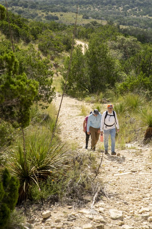 A group of people hike up a rocky trail at Hill Country State Natural Area