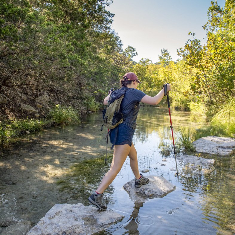 A woman walks on rocks while crossing a creek.