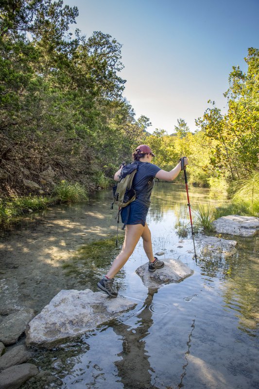 A woman walks on rocks while crossing a creek.