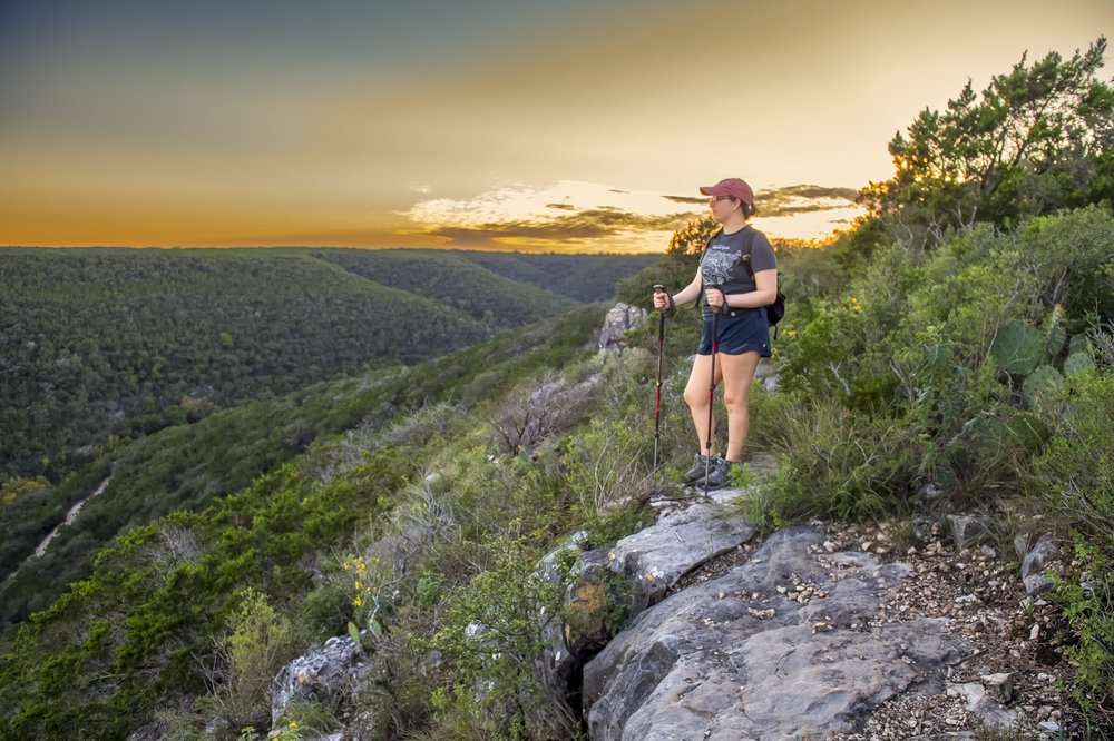A woman stands at an overlook enjoying the sunset.
