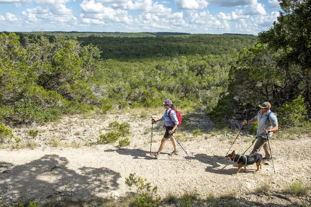 A man and woman hike along a trail with their dog at Pedernales Falls State Park