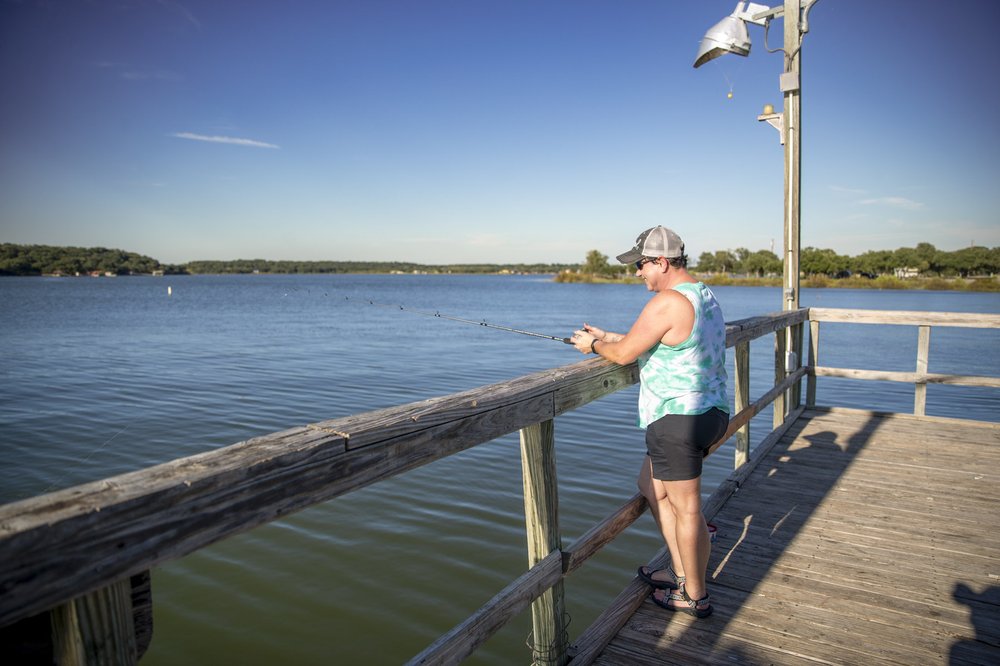 A woman wearing a hat and tank top fishing from the pier.