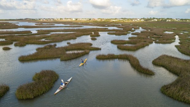 Two kayakers paddling through a marsh bayou