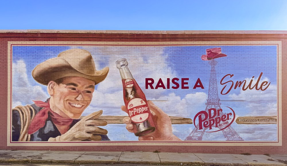 A mural of a cowboy reaching for a Dr Pepper bottled with the words "Raise a smile"