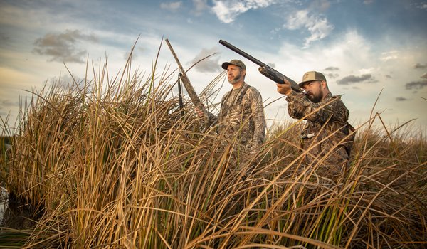 Two men in camoflauge hidden behind tall grass hunting.